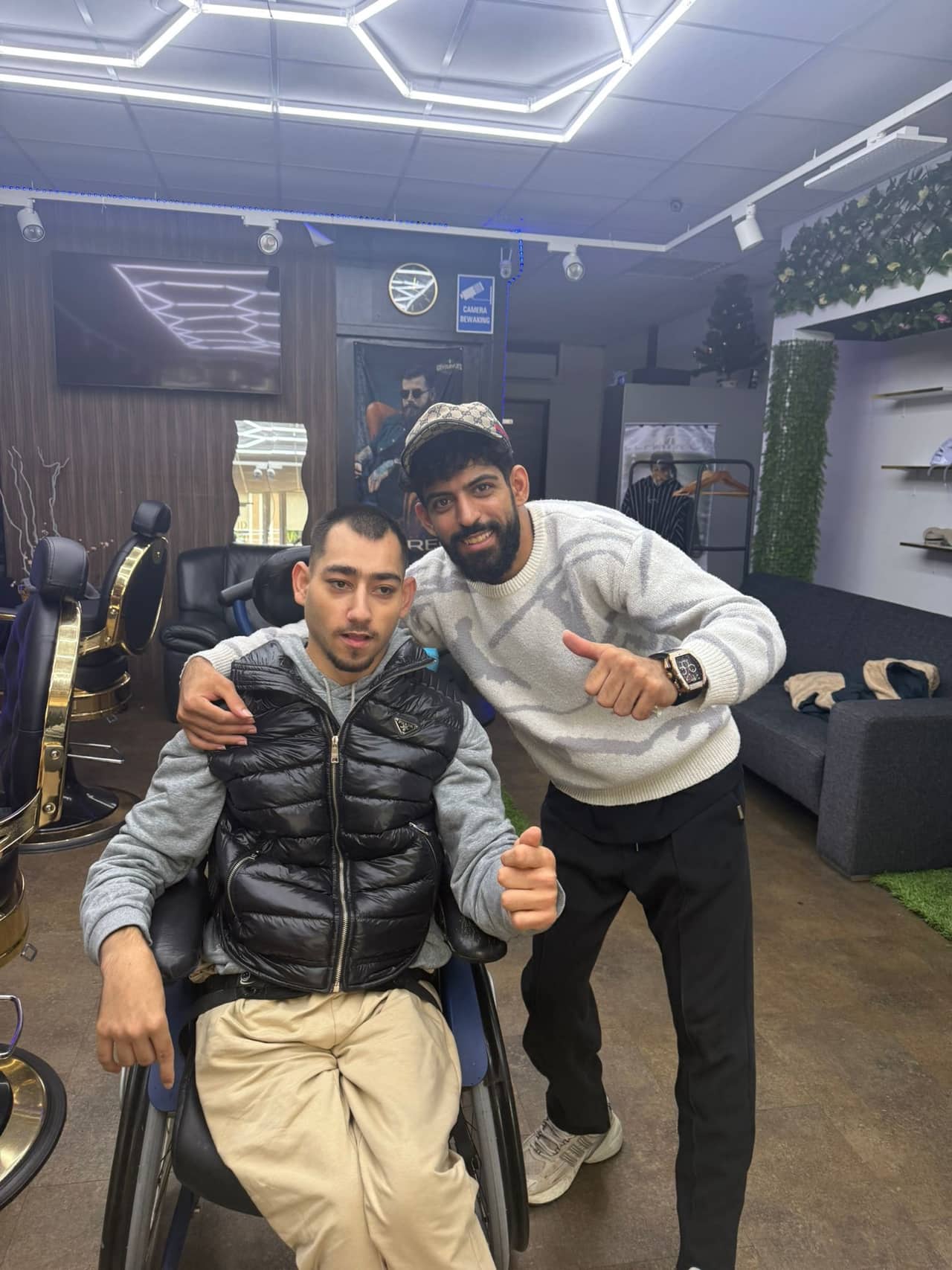 Ziayd staat naast een klant die in een rolstoel zit. Ze steken allebei hun duim op.